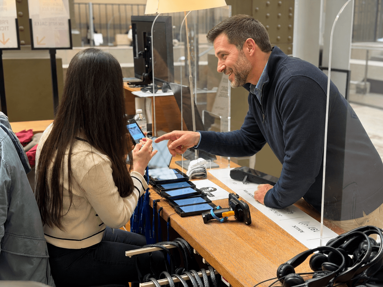 Museum staff member helping a visitor use an audio guide at a handout desk